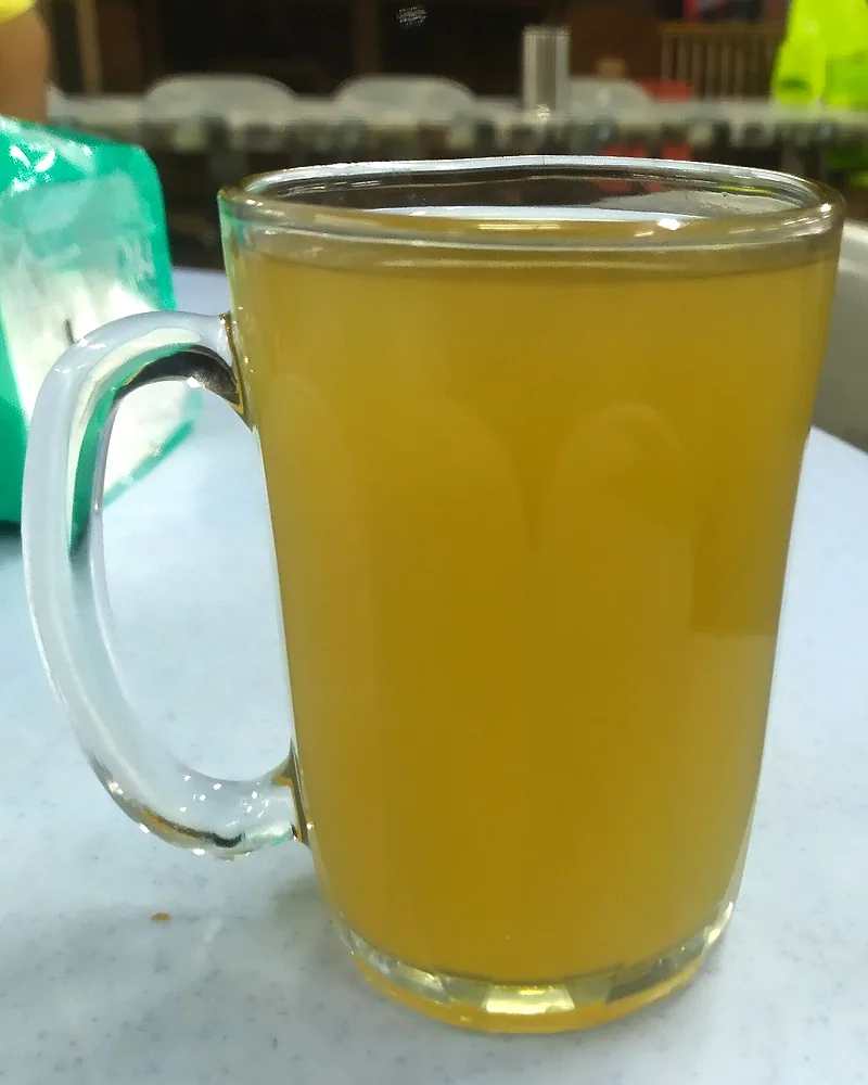 Segelas kunyit asam berwarna kuning cerah di atas meja