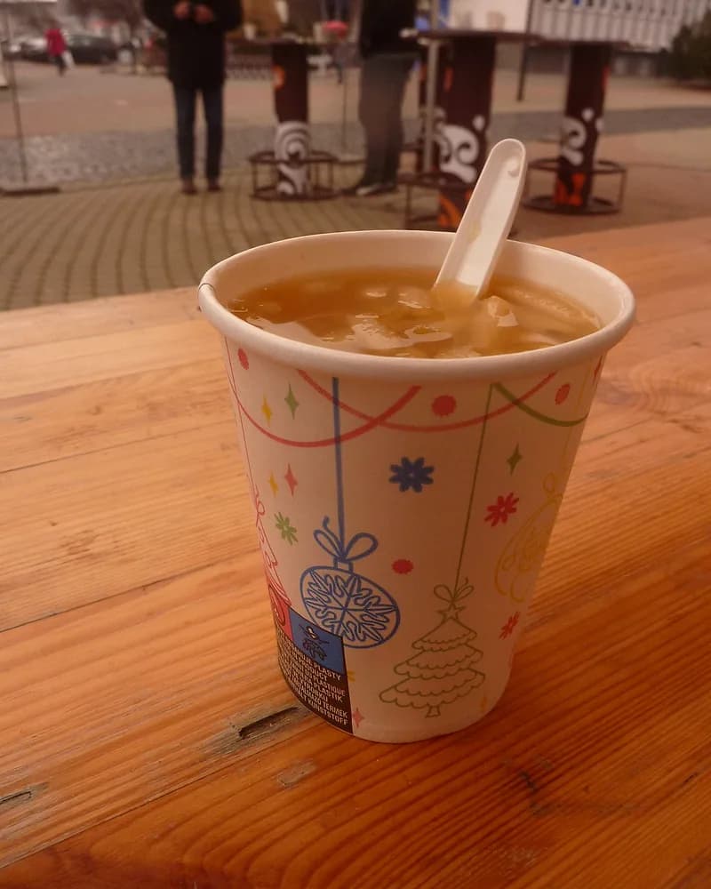 Segelas wedang rempah hangat dalam cup kertas di atas meja kayu
