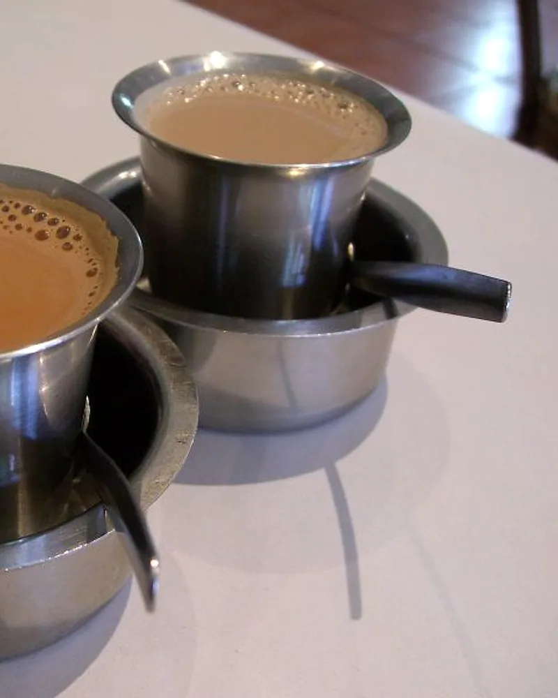 Teh rempah dalam gelas logam bersama alat penyaring kopi
